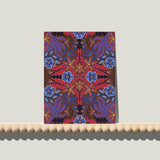 Enkele A6-kaart van Studio LilaLine met een symmetrische bloemenprint op de voorkant – het ontwerp toont spiegelende bloemvormen in diepe blauwtinten met accenten van rood. De vormen zijn sierlijk en ritmisch, alsof twee bloemen tegenover elkaar in een dans zijn bevroren. De kleuren geven de kaart een levendige maar toch harmonieuze uitstraling. Op de achterkant is ruimte voor een persoonlijke boodschap.