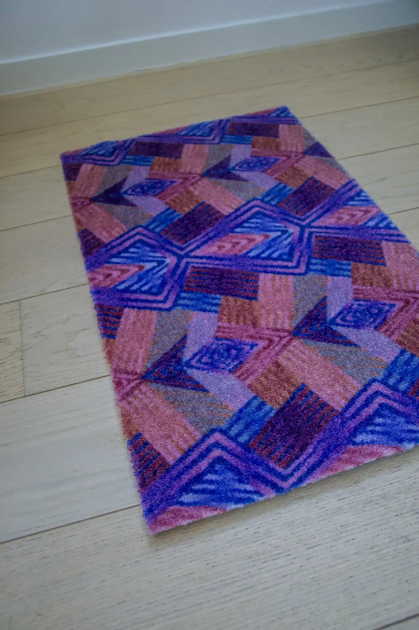 Zachte, goed absorberende badmat van Studio LilaLine met een grafisch diamantpatroon in paarse en roze tinten – de vormen zijn ritmisch en speels, met een vrolijke retro-uitstraling. De kleuren zorgen voor een warme, levendige sfeer in de badkamer. Heerlijk comfortabel onder je voeten na het douchen.