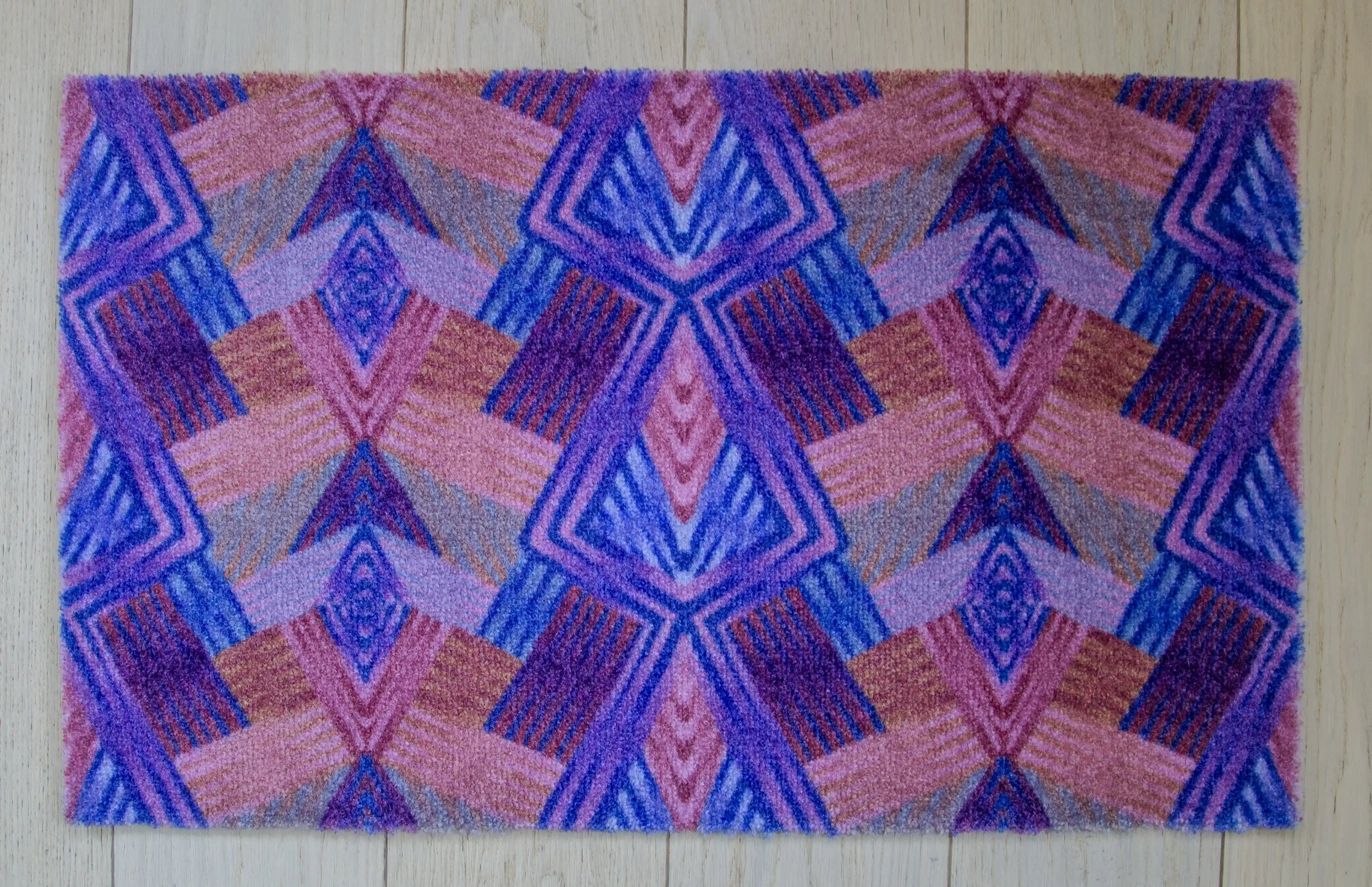 Zachte, goed absorberende badmat van Studio LilaLine met een grafisch diamantpatroon in paarse en roze tinten – de vormen zijn ritmisch en speels, met een vrolijke retro-uitstraling. De kleuren zorgen voor een warme, levendige sfeer in de badkamer. Heerlijk comfortabel onder je voeten na het douchen.