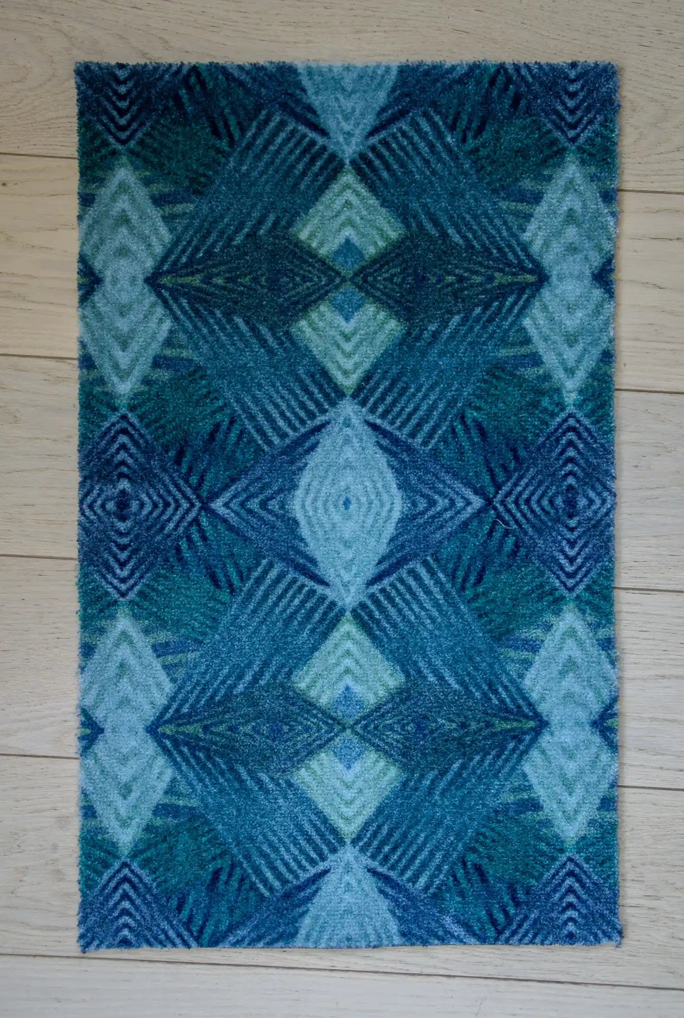 Zachte, waterabsorberende badmat van Studio LilaLine met een grafisch diamantpatroon in tinten petrol, blauw en groen – het ontwerp bestaat uit ritmische lijnen en geometrische vormen die samen een kalme, frisse uitstraling geven. De mat voelt aangenaam onder blote voeten en brengt kleur en stijl in de badkamer.