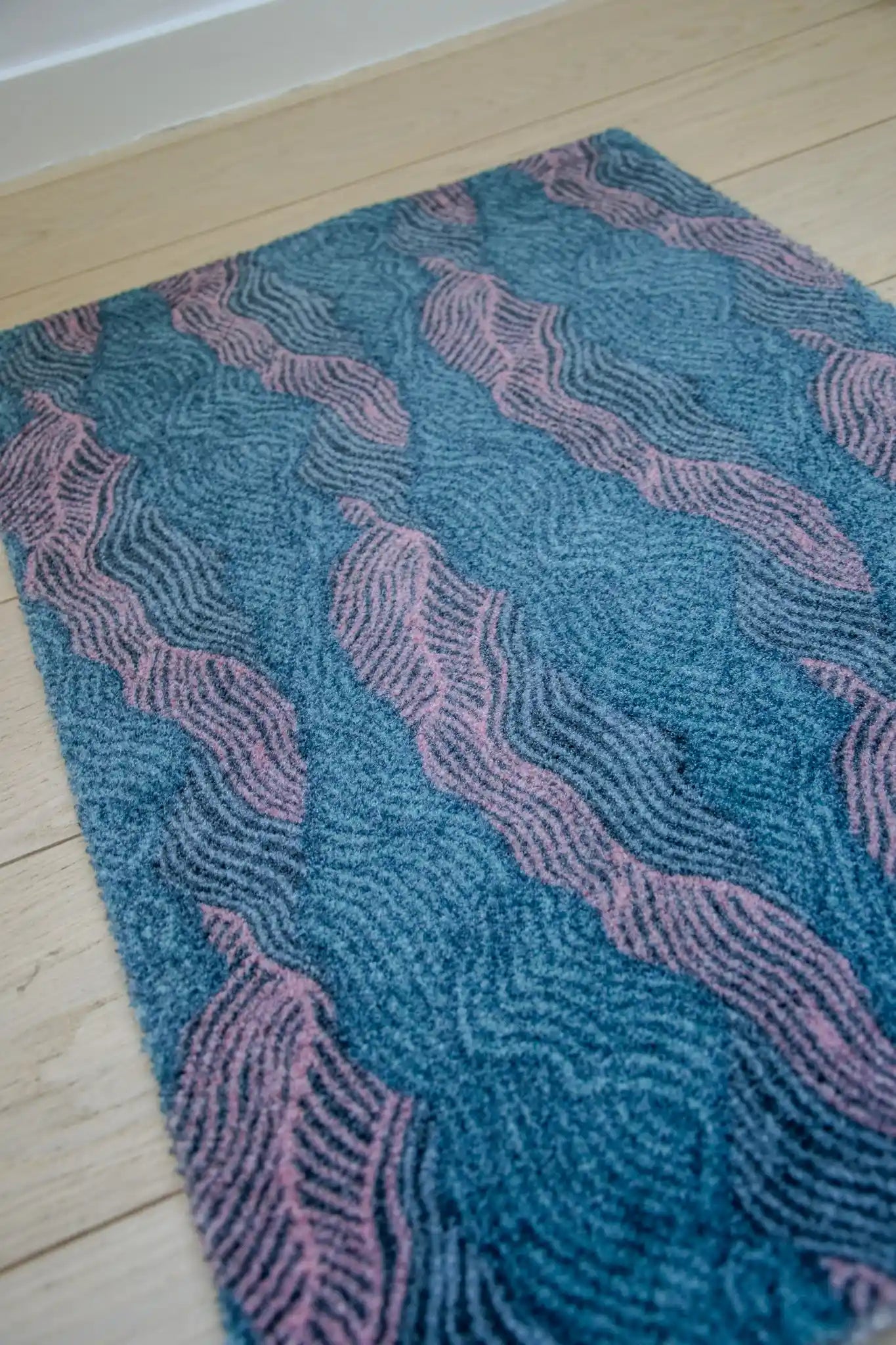 Zachte, waterabsorberende badmat van Studio LilaLine met een golvend patroon in roze en petrol – het ontwerp bestaat uit vloeiende lijnen die elkaar afwisselen als een rustige zeebeweging. De combinatie van frisse en warme kleuren geeft een ontspannen en toch speels gevoel. De mat voelt zacht aan en maakt je badkamer direct een stukje vrolijker.