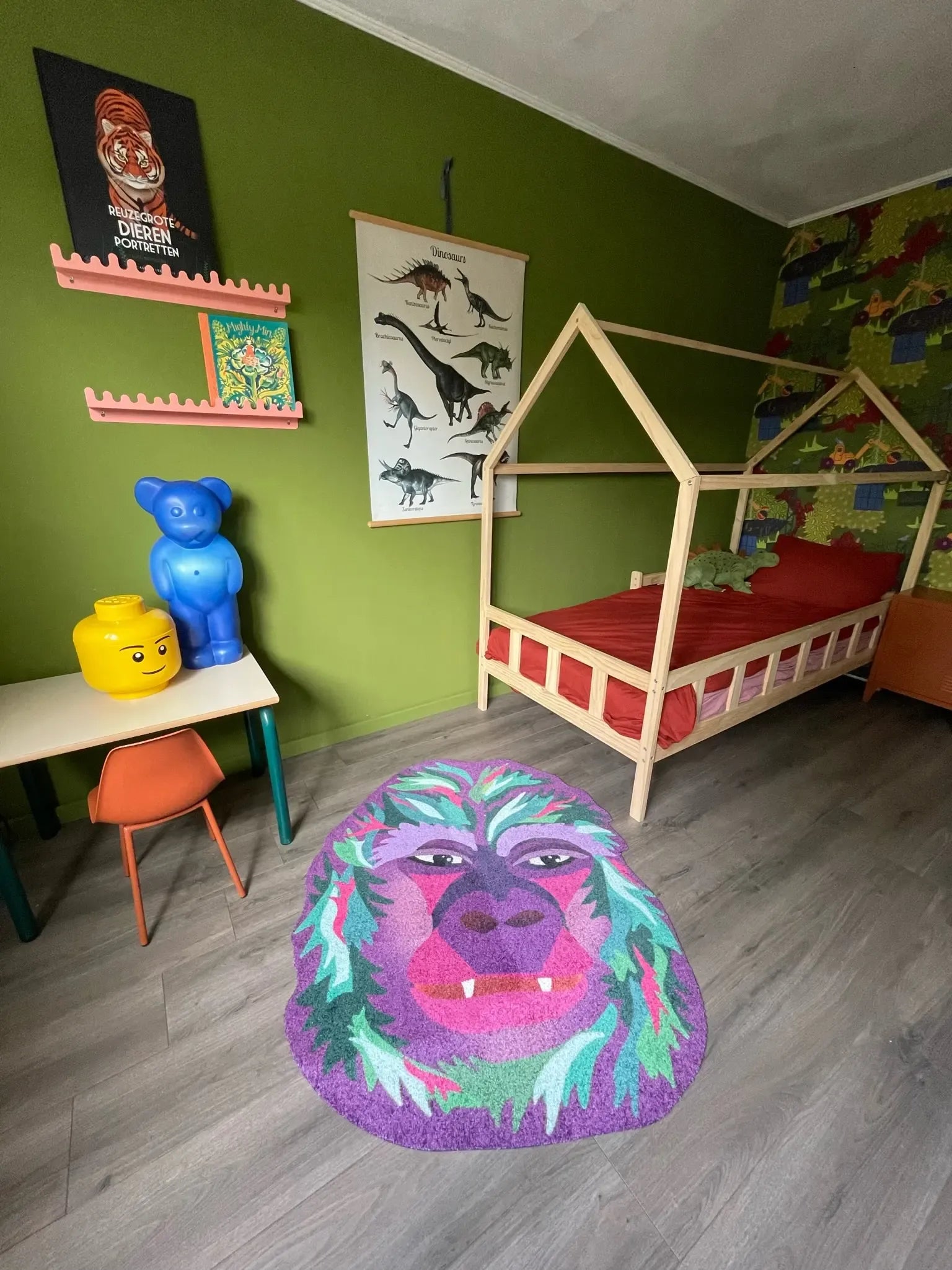 Zacht uitgesneden dierenkleed in de vorm van een gorillahoofd van Studio LilaLine – dit kleed toont een vriendelijk, stoer gorillagezicht in paars- en groentinten, met duidelijke gelaatstrekken zoals een brede kaaklijn, neus en intense ogen. De kleuren geven het dier een fantasierijke, bijna magische uitstraling. Heerlijk zacht om op te spelen of op te liggen in een kinderkamer of knusse hoek.