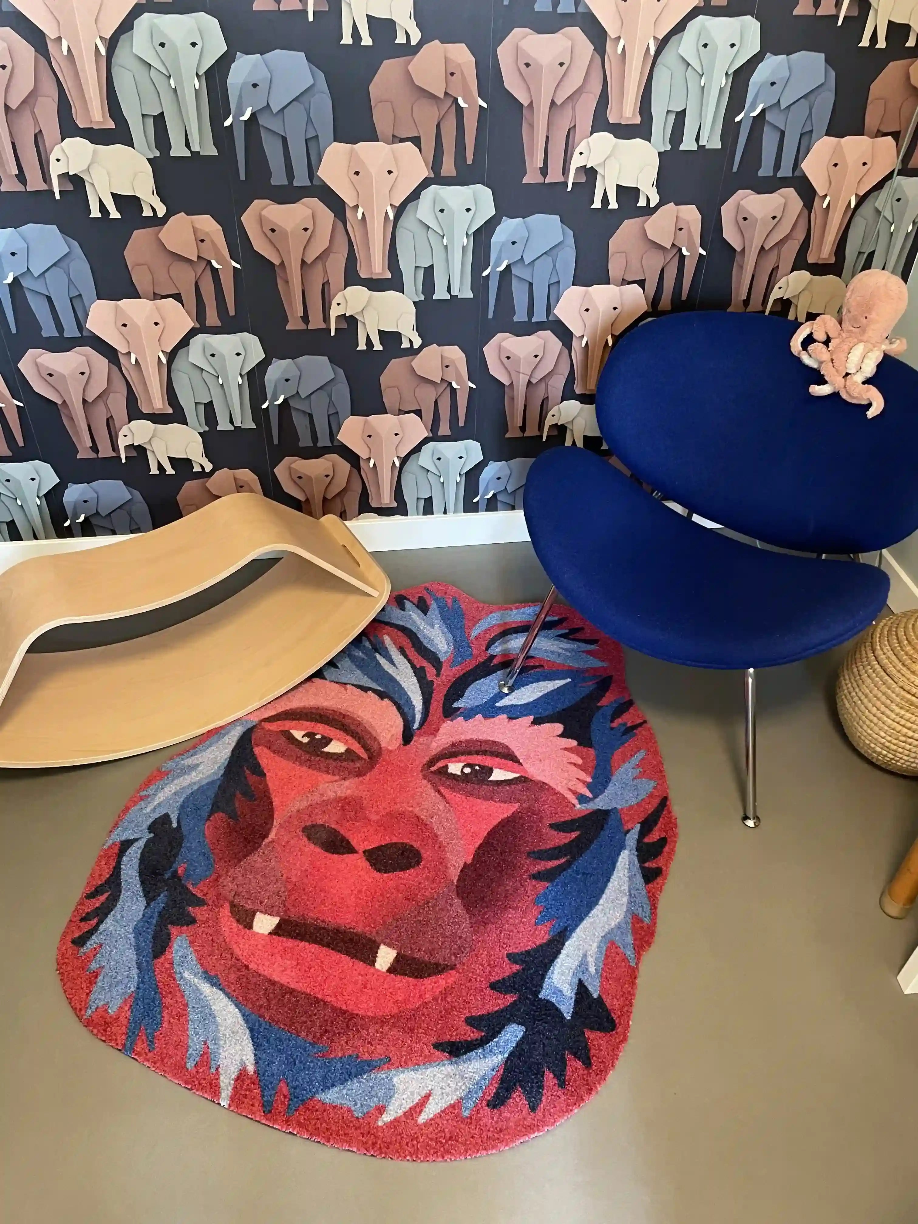 Zacht uitgesneden dierenkleed in de vorm van een gorillahoofd van Studio LilaLine – het kleed toont een krachtige, vriendelijke gorilla met een expressieve blik, uitgevoerd in diepe rood- en blauwtinten. De vorm is rond en herkenbaar, met duidelijke gelaatstrekken zoals een brede neus en zachte ogen. Een stoere en toch knusse speelplek voor op de vloer van een kinderkamer of speelhoek.