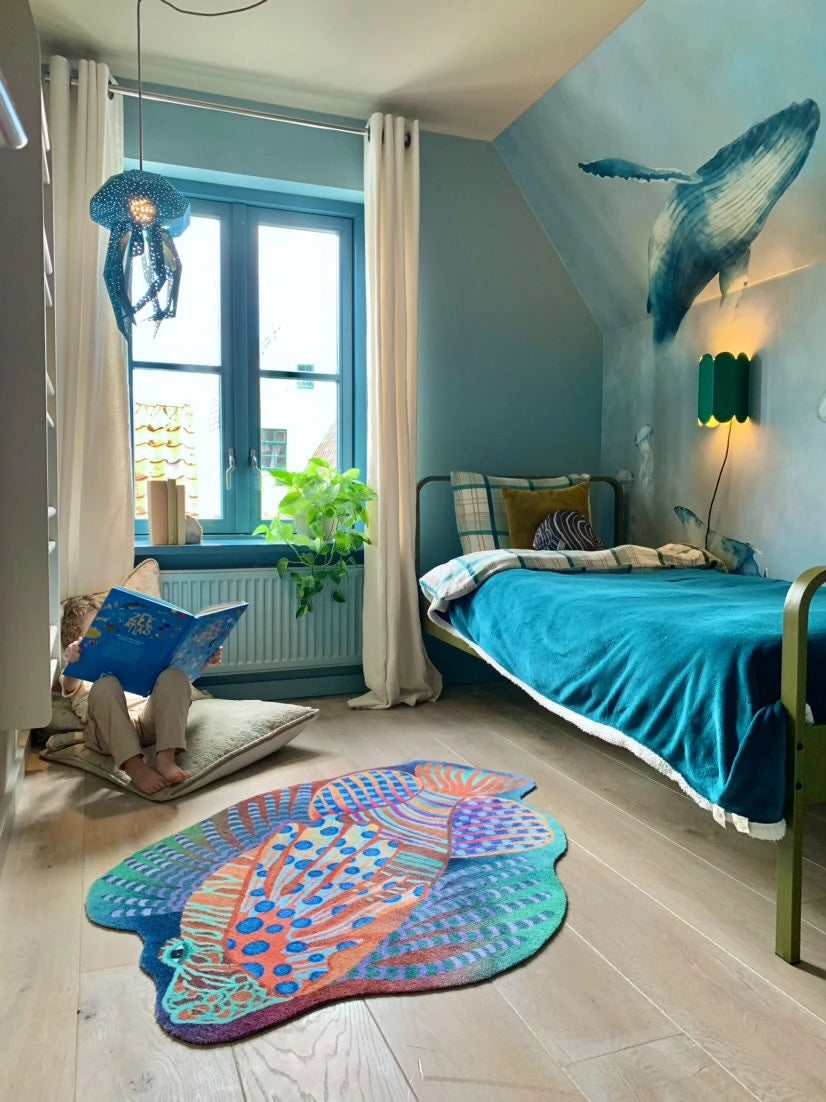 Zacht uitgesneden dierenkleed in de vorm van een koraalduivel van Studio LilaLine – deze fantasierijke vis heeft sierlijke vinnen die wijd uitstaan, in sprekende tinten groen en oranje. De visvorm is dynamisch en decoratief, met speelse strepen en zachte rondingen. Het kleed is heerlijk zacht en nodigt uit tot spelen, liggen of fantaseren in een gezellige hoek van de kinderkamer.