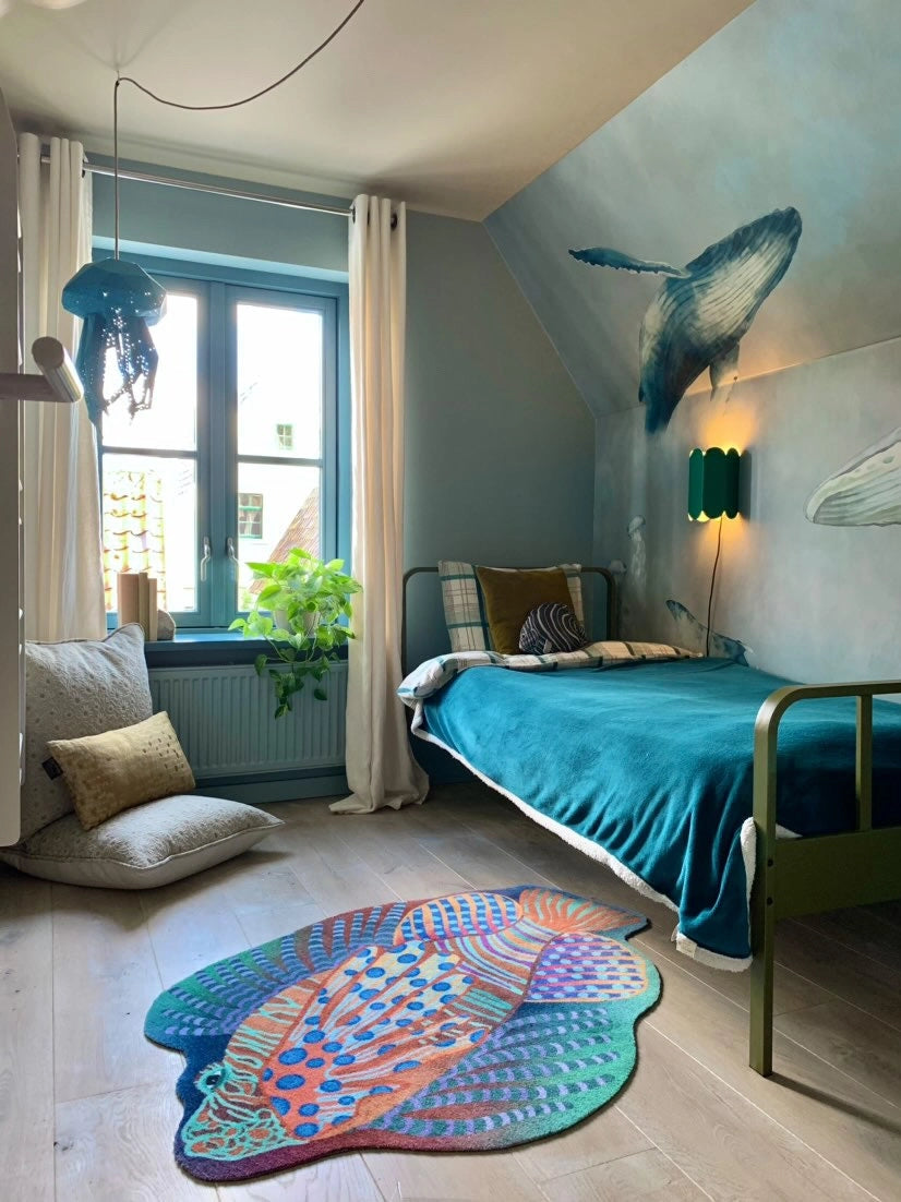 Zacht uitgesneden dierenkleed in de vorm van een koraalduivel van Studio LilaLine – deze fantasierijke vis heeft sierlijke vinnen die wijd uitstaan, in sprekende tinten groen en oranje. De visvorm is dynamisch en decoratief, met speelse strepen en zachte rondingen. Het kleed is heerlijk zacht en nodigt uit tot spelen, liggen of fantaseren in een gezellige hoek van de kinderkamer.