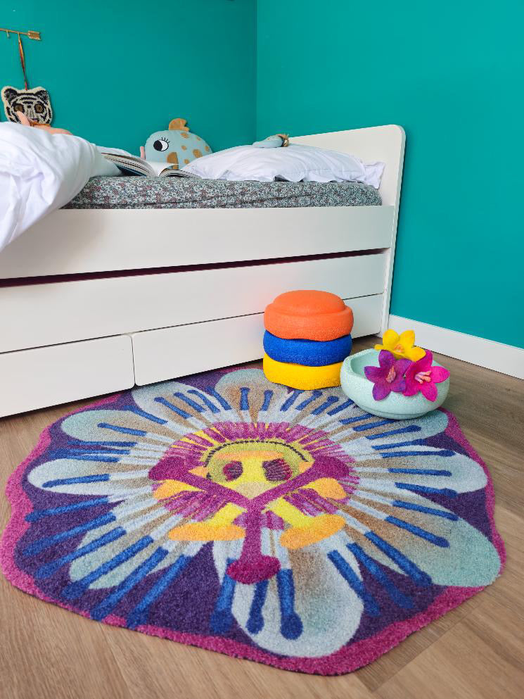 Zacht uitgesneden kleed in de vorm van een passiebloem van Studio LilaLine – het kleed toont een ronde bloem met fijne, uitgesneden bloemblaadjes in blauw, paars en geel. Het hart van de bloem is gedetailleerd en lijkt bijna te stralen, met lagen die doen denken aan zonnestralen of franjes. De vorm is symmetrisch en sierlijk. Heerlijk zacht en perfect om op te spelen, te zitten of gewoon als vrolijk accent in een kinderkamer.