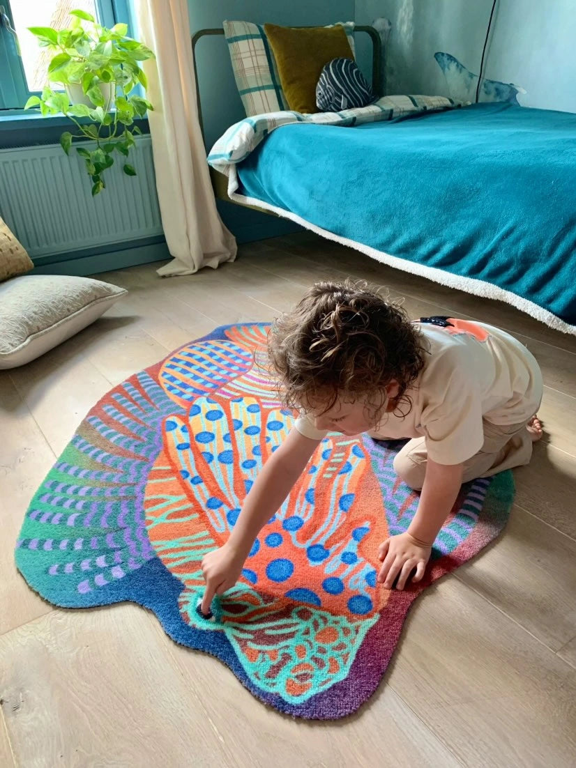 Zacht uitgesneden dierenkleed in de vorm van een koraalduivel van Studio LilaLine – deze fantasierijke vis heeft sierlijke vinnen die wijd uitstaan, in sprekende tinten groen en oranje. De visvorm is dynamisch en decoratief, met speelse strepen en zachte rondingen. Het kleed is heerlijk zacht en nodigt uit tot spelen, liggen of fantaseren in een gezellige hoek van de kinderkamer.