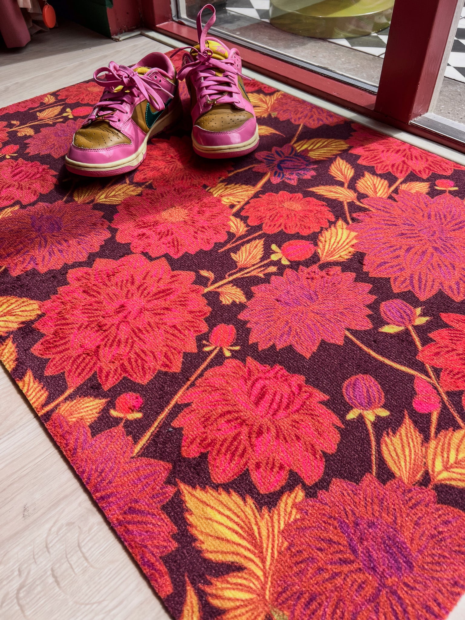 Droogloopmat met dahlia’s in warme oranje- en roodtinten op een bordeauxrode ondergrond. Een rijke en sfeervolle herfstmat voor een warme entree.