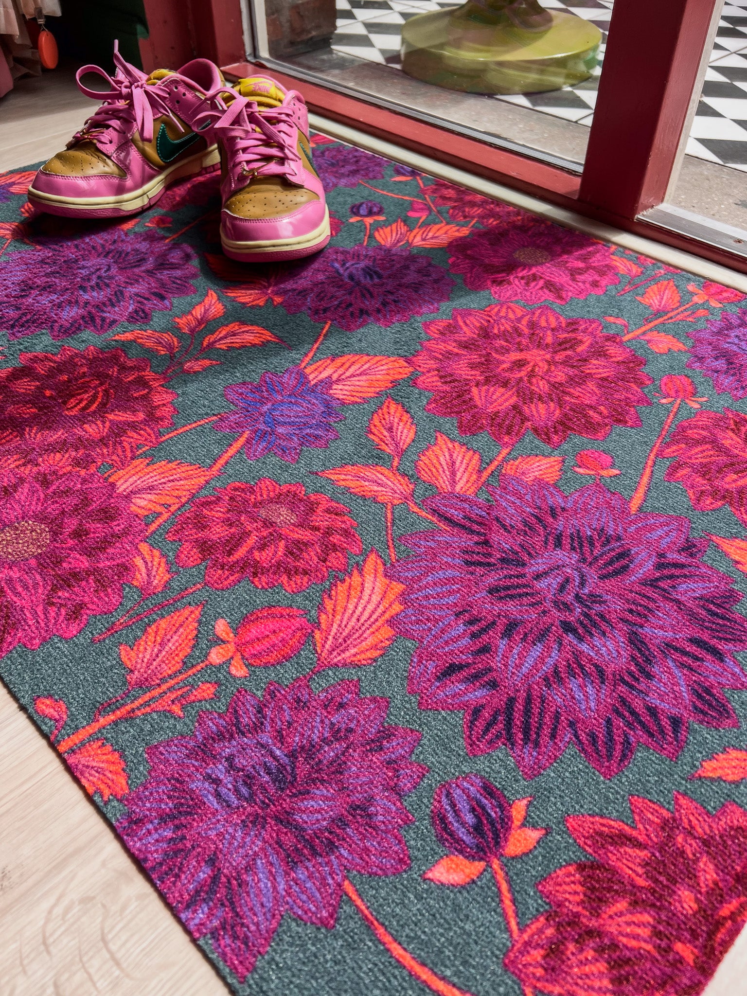 Droogloopmat met grote dahlia's in paars, roze en rood op een diepe petrolkleur. Een uitbundige bloemenprint vol zomerse energie.