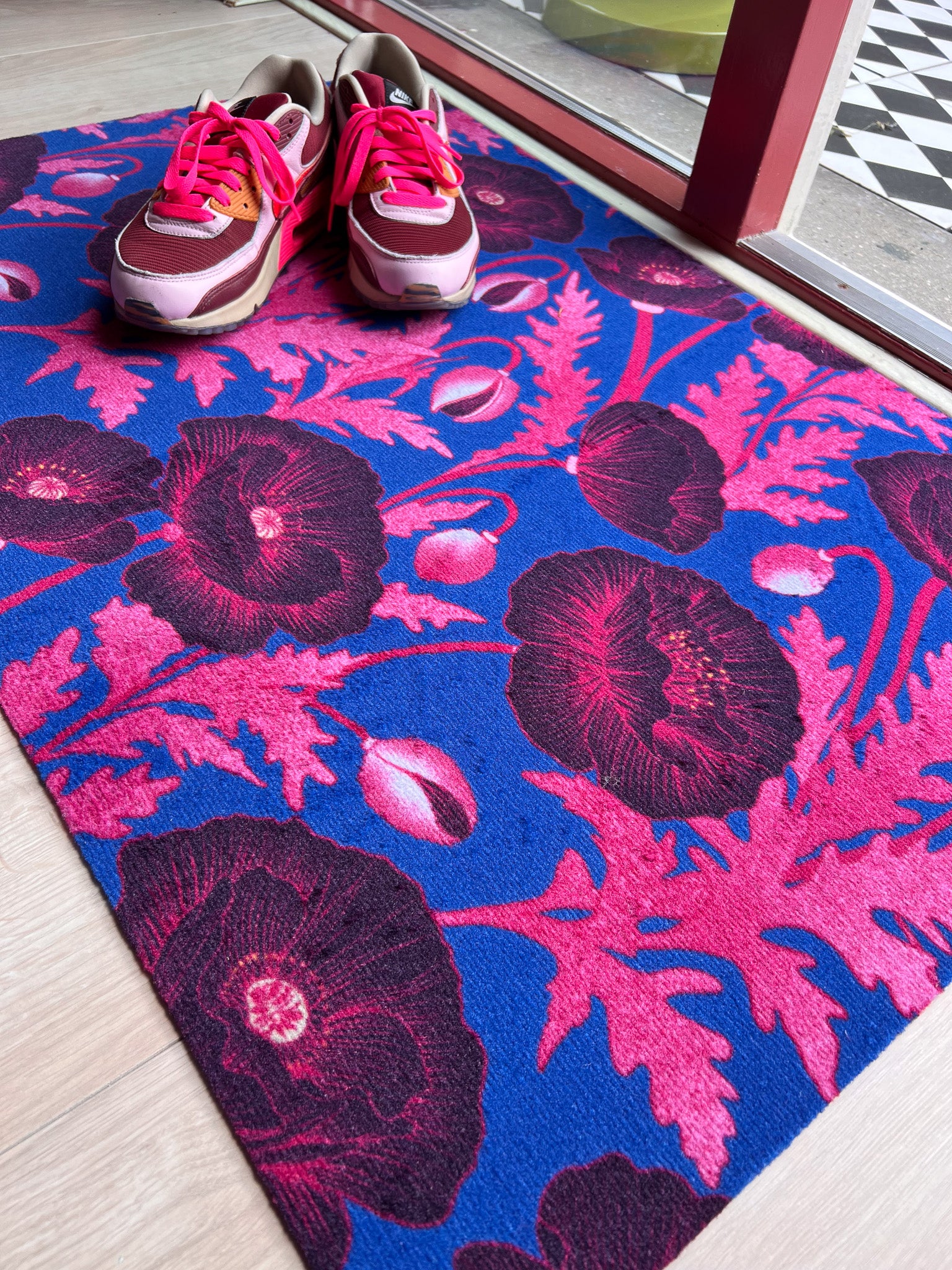 Droogloopmat met roze klaprozen die oplichten tegen een felblauwe achtergrond. Een verrassende winterprint vol kleur en optimisme.