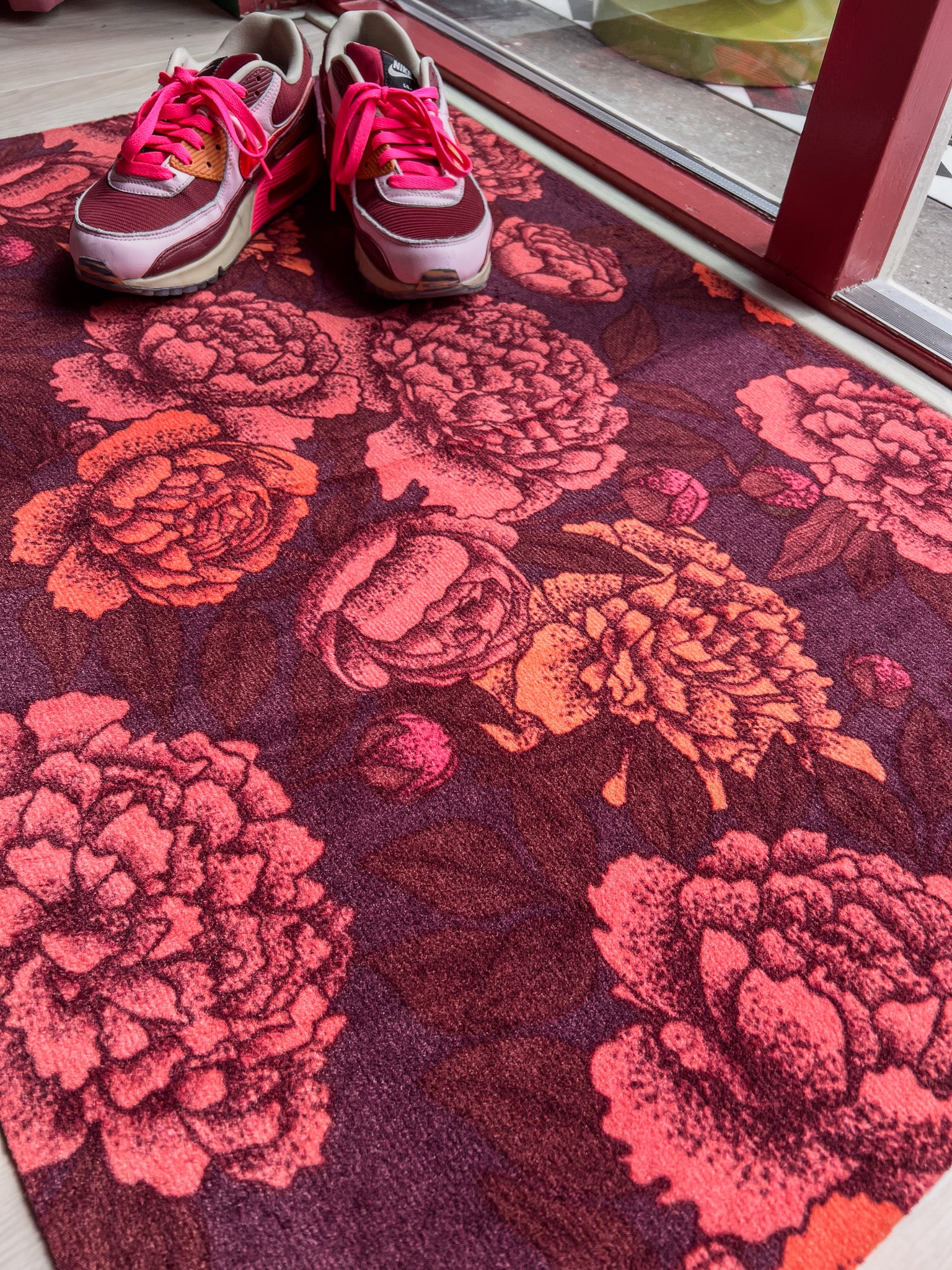 Droogloopmat met warme pioenrozen in koraal en oranje op een bordeauxrode ondergrond. Ideaal voor een gezellige en knusse herfstsfeer in huis.