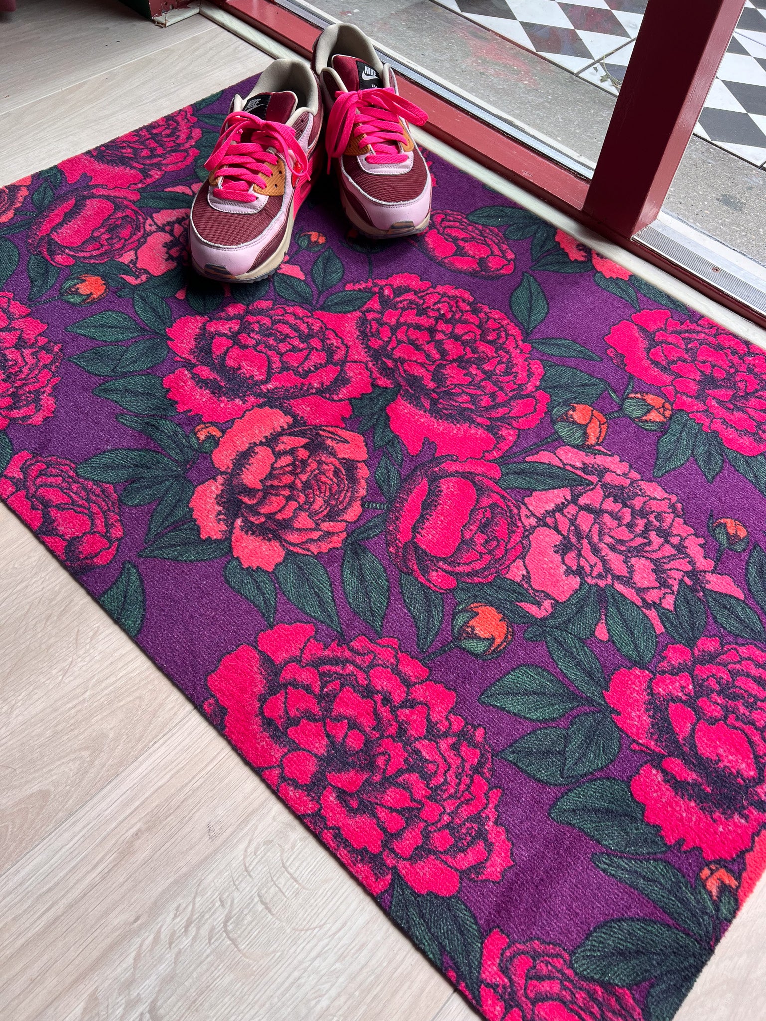 Droogloopmat met uitbundige felroze pioenrozen op een diepe paarse achtergrond. Een vrolijke, zomerse bloemenmat vol energie en kleur.