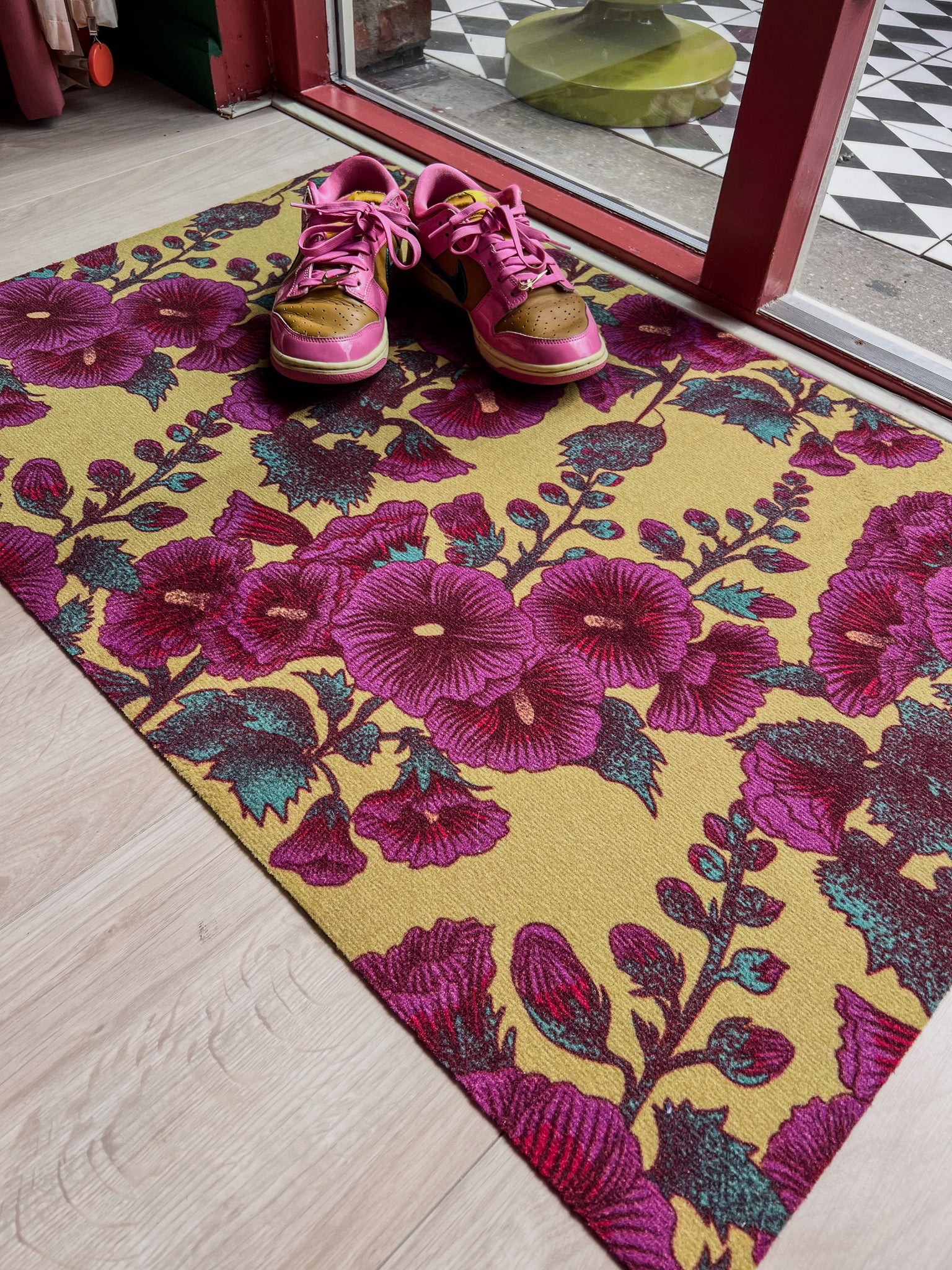 Droogloopmat met roze stokrozen op een warme okergele achtergrond. Een vrolijke lentemix die meteen zon en bloemen de hal binnenbrengt.