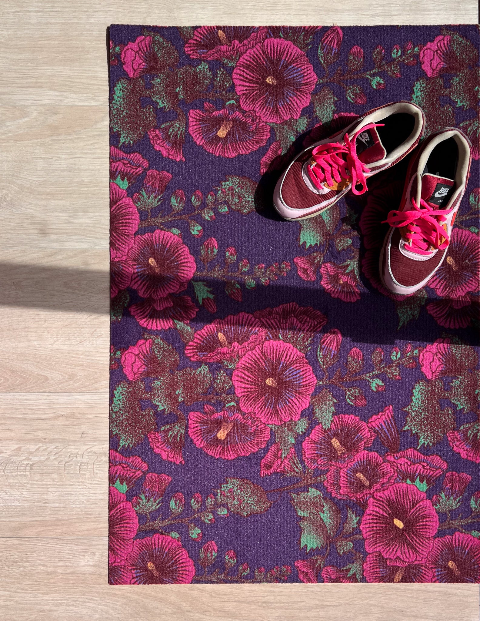 Droogloopmat met roze stokrozen op een diepe paarse ondergrond. Een rijke, zomerse print vol charme en contrast.