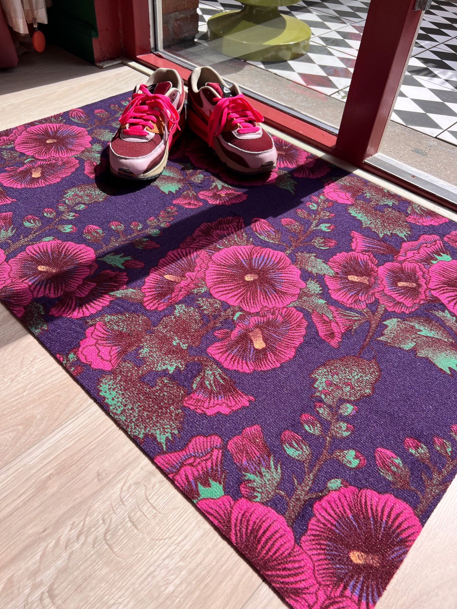 Droogloopmat met roze stokrozen op een diepe paarse ondergrond. Een rijke, zomerse print vol charme en contrast.