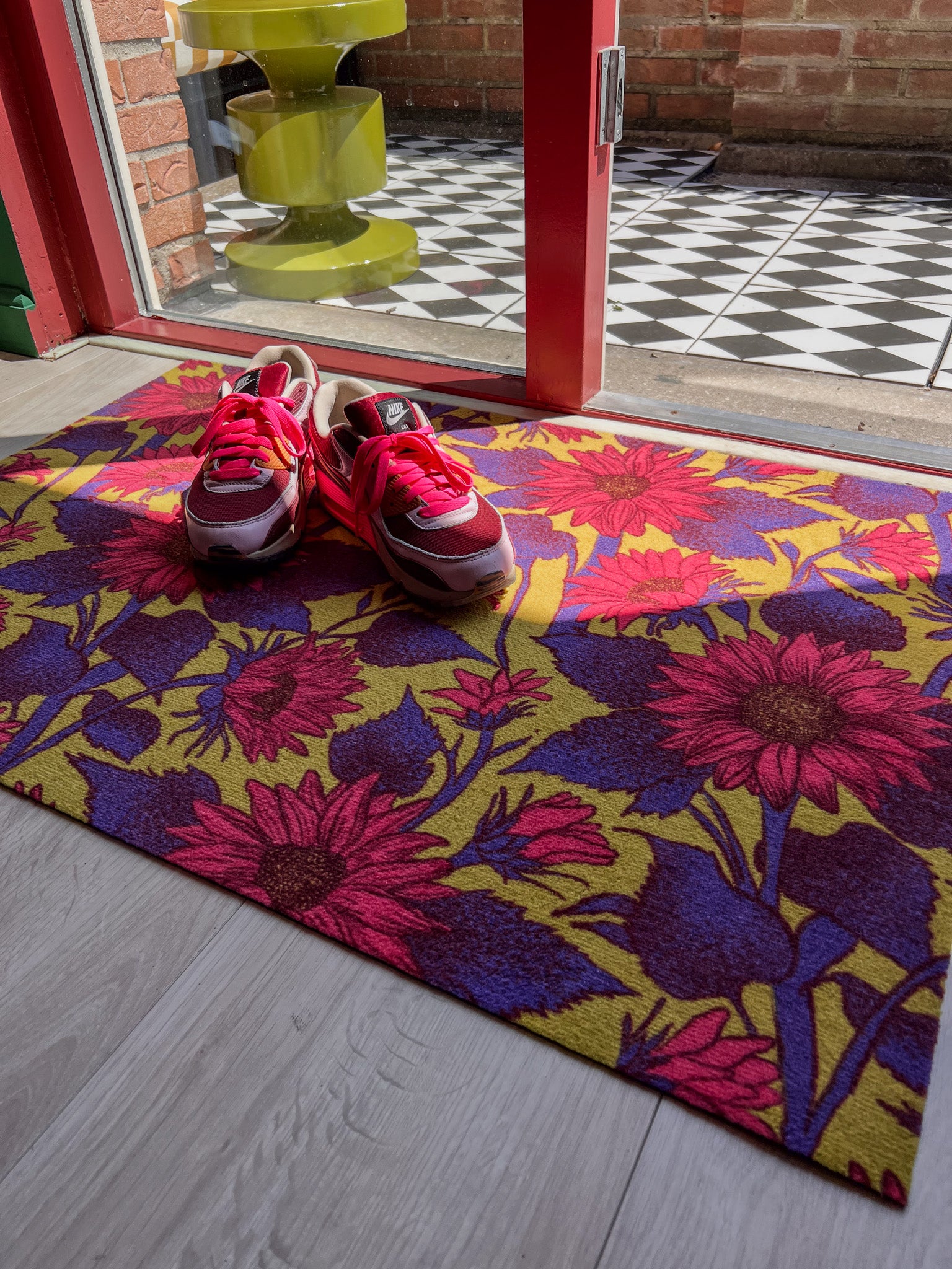 Droogloopmat met felroze zonnebloemen op een mosterdgroene achtergrond. De vrolijke bloemenprint geeft een frisse lentesfeer en maakt de entree warm en uitnodigend.