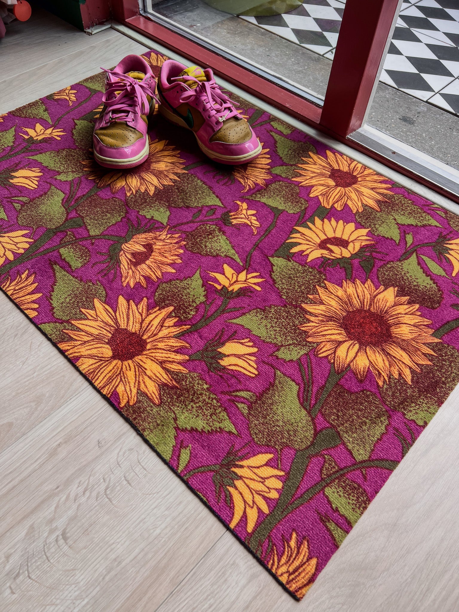 Droogloopmat met grote zonnebloemen in warme tinten op een levendige fuchsia ondergrond. Een zomerse kleurenexplosie voor bij de voordeur.