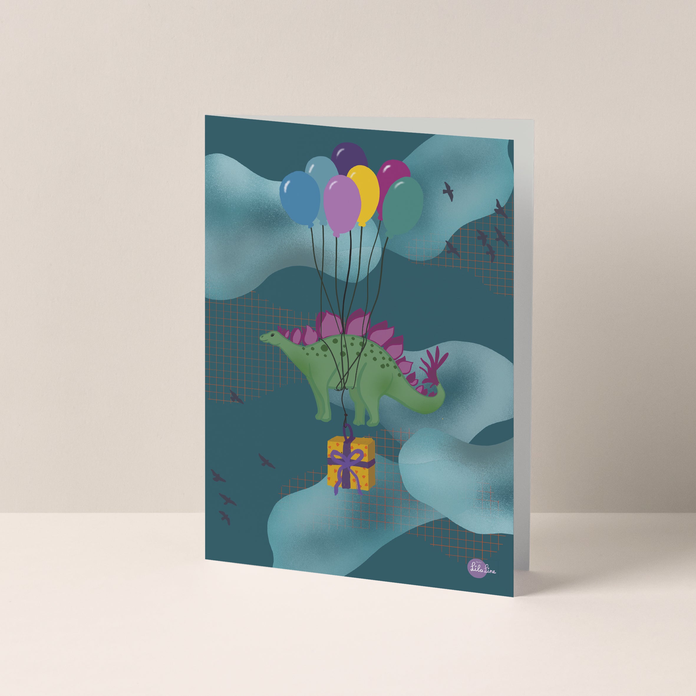 Dubbelgevouwen A6-kaart van Studio LilaLine met op de voorkant een stegosaurus die door de lucht zweeft dankzij een tros kleurrijke ballonnen die op zijn rug zijn vastgebonden – onder hem bungelt een cadeau aan een lint. De illustratie is vrolijk, fantasierijk en feestelijk, perfect voor een verjaardagskaart. De binnenkant is leeg en biedt ruimte voor een persoonlijke boodschap.