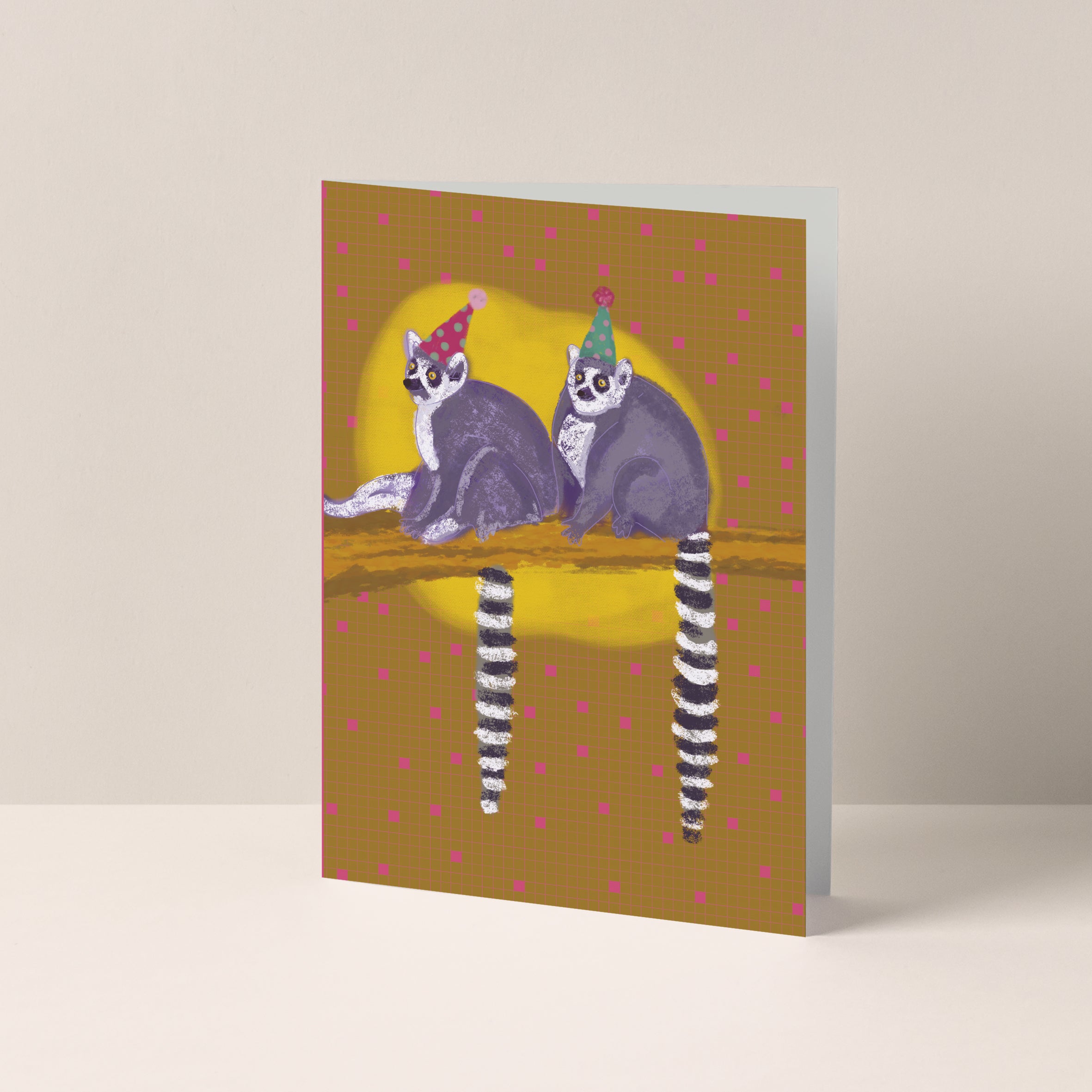 Dubbelgevouwen A6-kaart van Studio LilaLine met op de voorkant twee maki’s – herkenbaar aan hun lange, gestreepte staarten – die samen op een tak zitten met feestmutsjes op. Ze kijken vrolijk en ondeugend, klaar om een feestje te vieren. De illustratie is kleurrijk en speels, perfect voor een verjaardagskaart. De binnenkant is blanco en klaar voor een persoonlijke boodschap.
