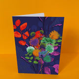 Dubbelgevouwen luxe A5-kaart van Studio LilaLine met op de voorkant een krachtige dahlia in donkerblauw, met accenten van rood en groen – de bloem is groot en gelaagd, met bloemblaadjes die als golven naar buiten krullen. De kleuren geven de kaart een intense, bijna koninklijke uitstraling. De binnenkant is blanco en extra ruim, perfect voor een persoonlijke boodschap met impact.