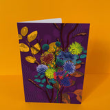 Dubbelgevouwen luxe A5-kaart van Studio LilaLine met op de voorkant een weelderige dahlia in tinten paars, blauw en geel – de bloem is groots en gelaagd, met bloemblaadjes die zich als een zonnebloem rond het hart uitvouwen. De kleuren zijn rijk en levendig, perfect om iemand op te fleuren of te verrassen. De binnenkant is royaal en blanco, ideaal voor een persoonlijke en uitgebreide boodschap.