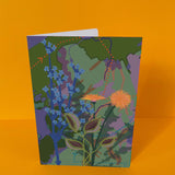 Dubbelgevouwen luxe A5-kaart van Studio LilaLine met op de voorkant een zachte illustratie van een paardenbloem in tinten groen, blauw en een vleugje geel – de bloem staat in volle pluim, met fijne lijnen die uitstralen alsof de zaadjes elk moment kunnen wegwaaien. De sfeer is teder en hoopvol. De binnenkant is blanco en ruim, perfect om iemand een liefdevolle of bemoedigende boodschap te schrijven.
