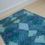 Zachte, waterabsorberende badmat van Studio LilaLine met een grafisch diamantpatroon in tinten petrol, blauw en groen – het ontwerp bestaat uit ritmische lijnen en geometrische vormen die samen een kalme, frisse uitstraling geven. De mat voelt aangenaam onder blote voeten en brengt kleur en stijl in de badkamer.