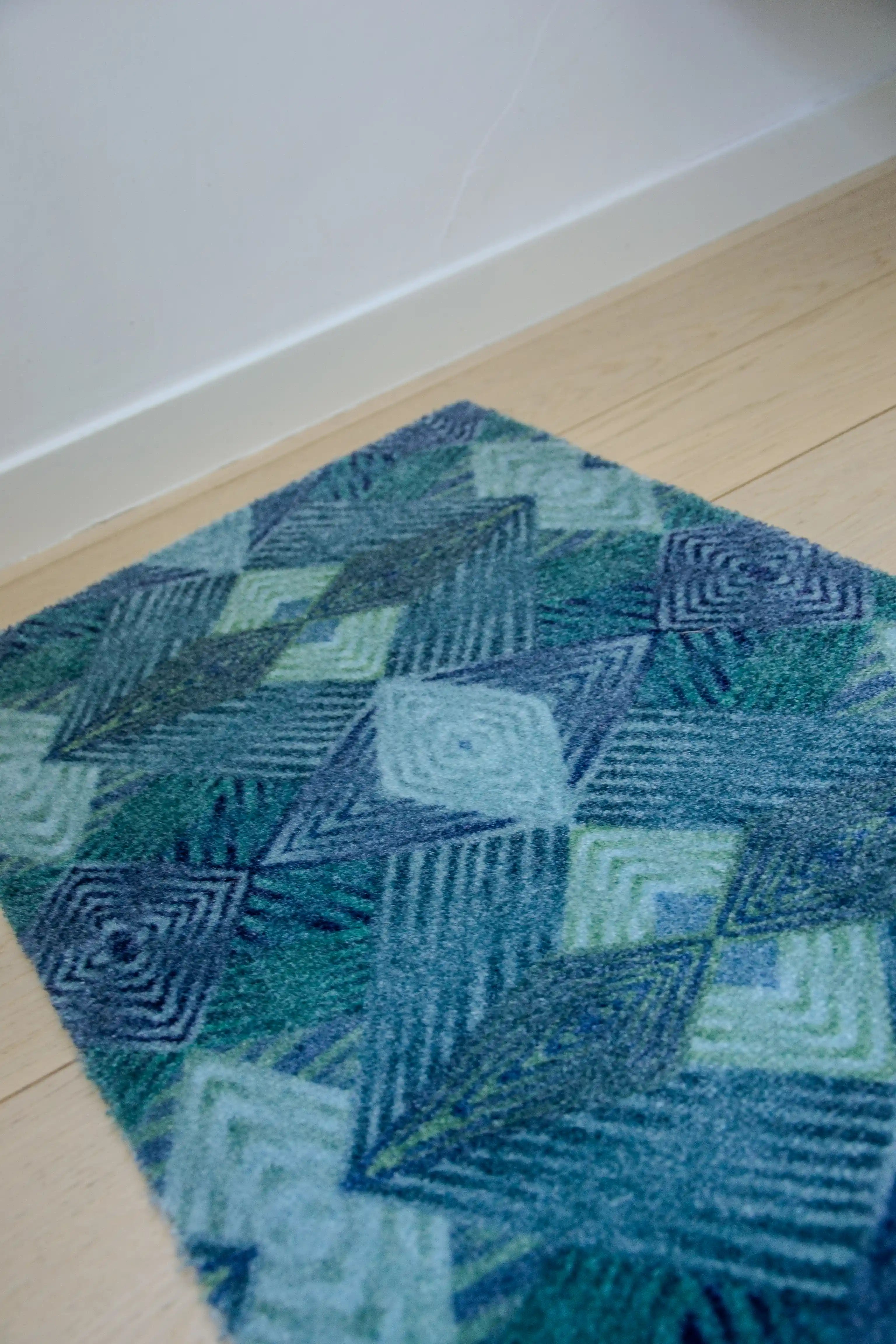 Zachte, waterabsorberende badmat van Studio LilaLine met een grafisch diamantpatroon in tinten petrol, blauw en groen – het ontwerp bestaat uit ritmische lijnen en geometrische vormen die samen een kalme, frisse uitstraling geven. De mat voelt aangenaam onder blote voeten en brengt kleur en stijl in de badkamer.