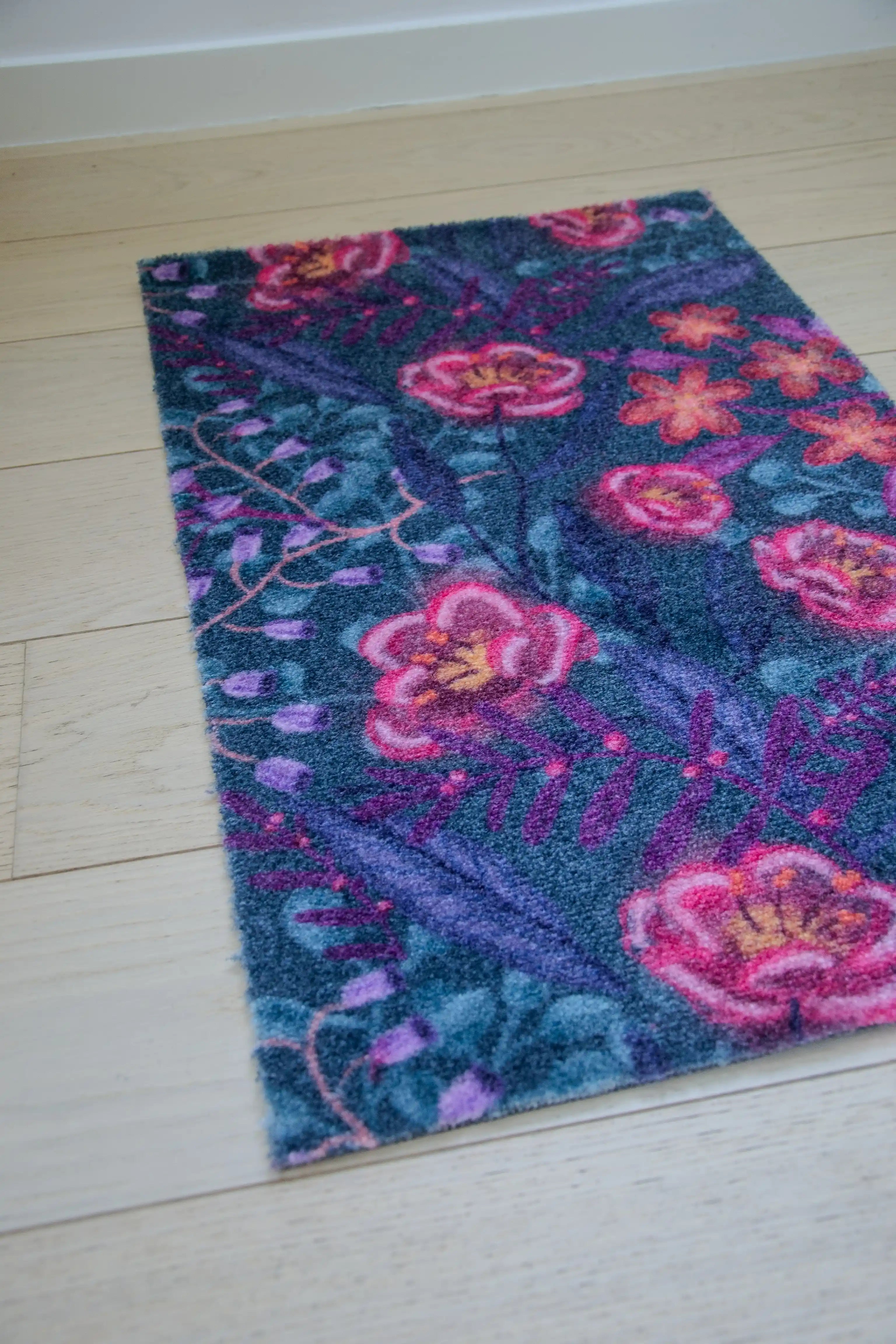 Zachte, waterabsorberende badmat van Studio LilaLine met een dromerige bloemenprint in diepe petroltinten, gecombineerd met accenten van roze en paars – het ontwerp straalt rust en elegantie uit, met sierlijke vormen die lijken te zweven over het oppervlak. De mat voelt heerlijk zacht aan en brengt een stijlvolle, ontspannen sfeer in de badkamer.