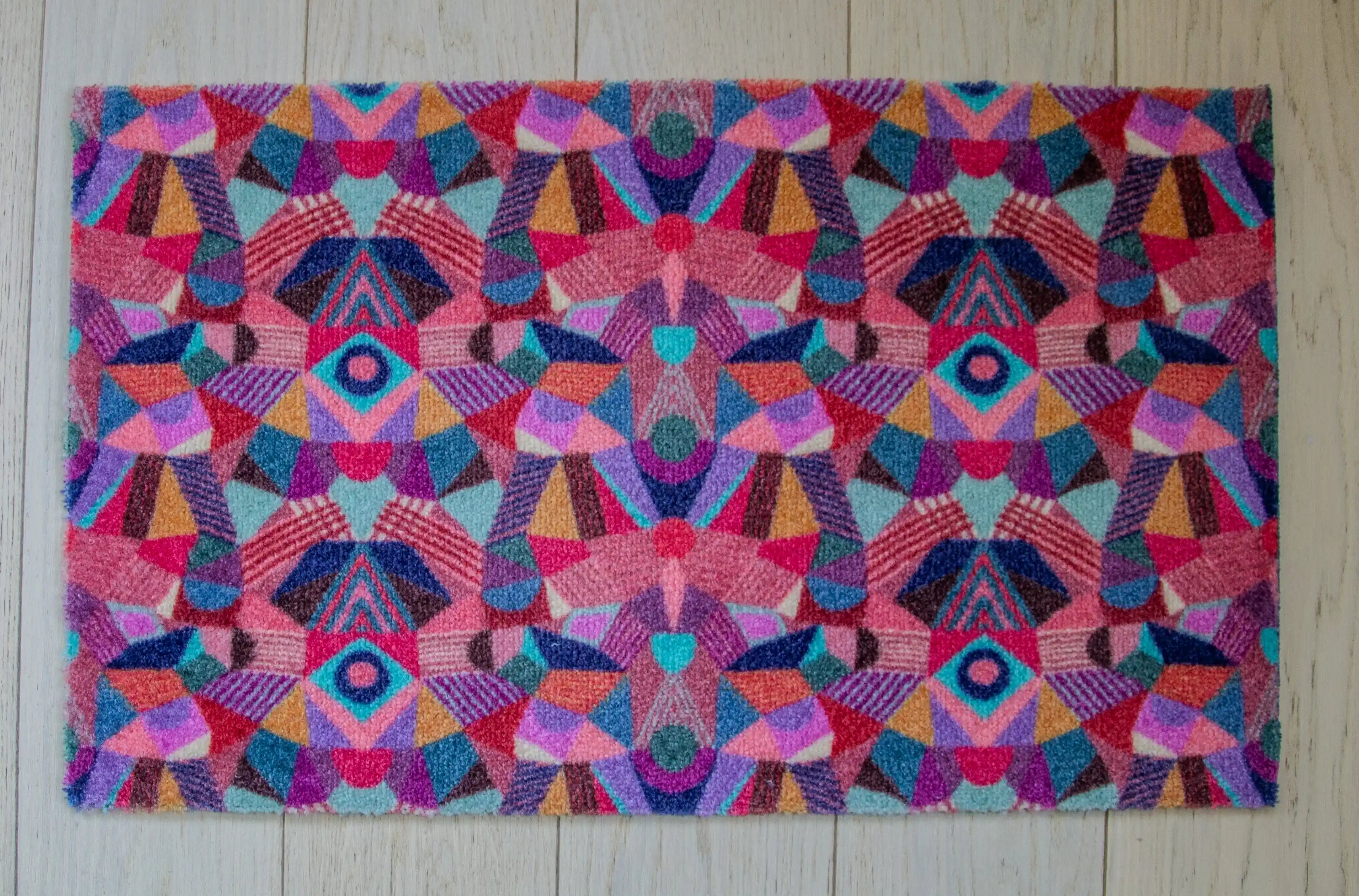 Zachte en goed absorberende badmat van Studio LilaLine met een kleurrijk patroon in roze, rood, groen en blauw – het ontwerp lijkt op de symmetrische patronen van een caleidoscoop, met speelse vormen die in lagen over elkaar draaien. De levendige kleuren maken deze mat een echte blikvanger in de badkamer. Heerlijk zacht voor je voeten na het douchen of badderen.
