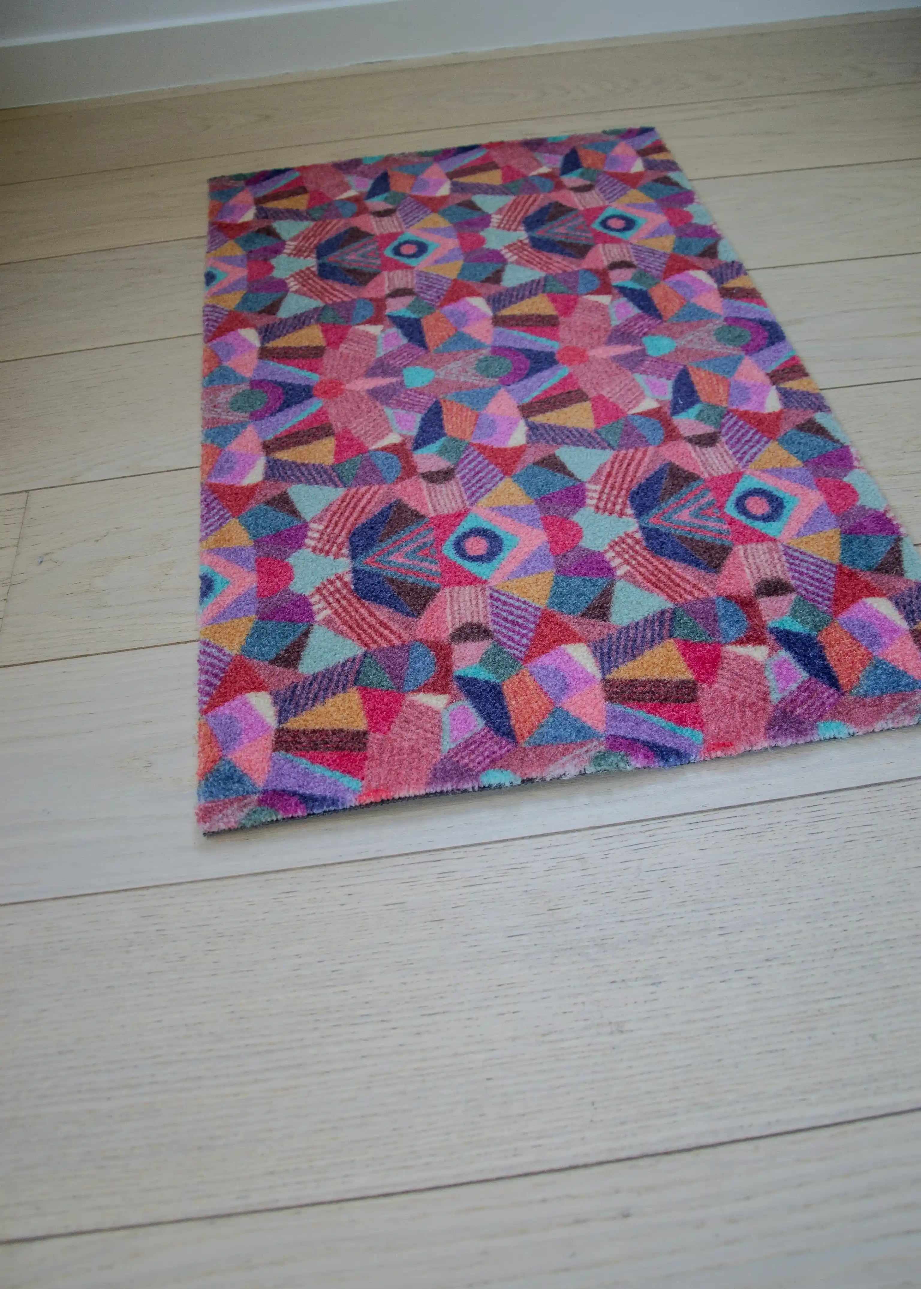 Zachte en goed absorberende badmat van Studio LilaLine met een kleurrijk patroon in roze, rood, groen en blauw – het ontwerp lijkt op de symmetrische patronen van een caleidoscoop, met speelse vormen die in lagen over elkaar draaien. De levendige kleuren maken deze mat een echte blikvanger in de badkamer. Heerlijk zacht voor je voeten na het douchen of badderen.