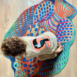 Zacht uitgesneden dierenkleed in de vorm van een koraalduivel van Studio LilaLine – deze fantasierijke vis heeft sierlijke vinnen die wijd uitstaan, in sprekende tinten groen en oranje. De visvorm is dynamisch en decoratief, met speelse strepen en zachte rondingen. Het kleed is heerlijk zacht en nodigt uit tot spelen, liggen of fantaseren in een gezellige hoek van de kinderkamer.