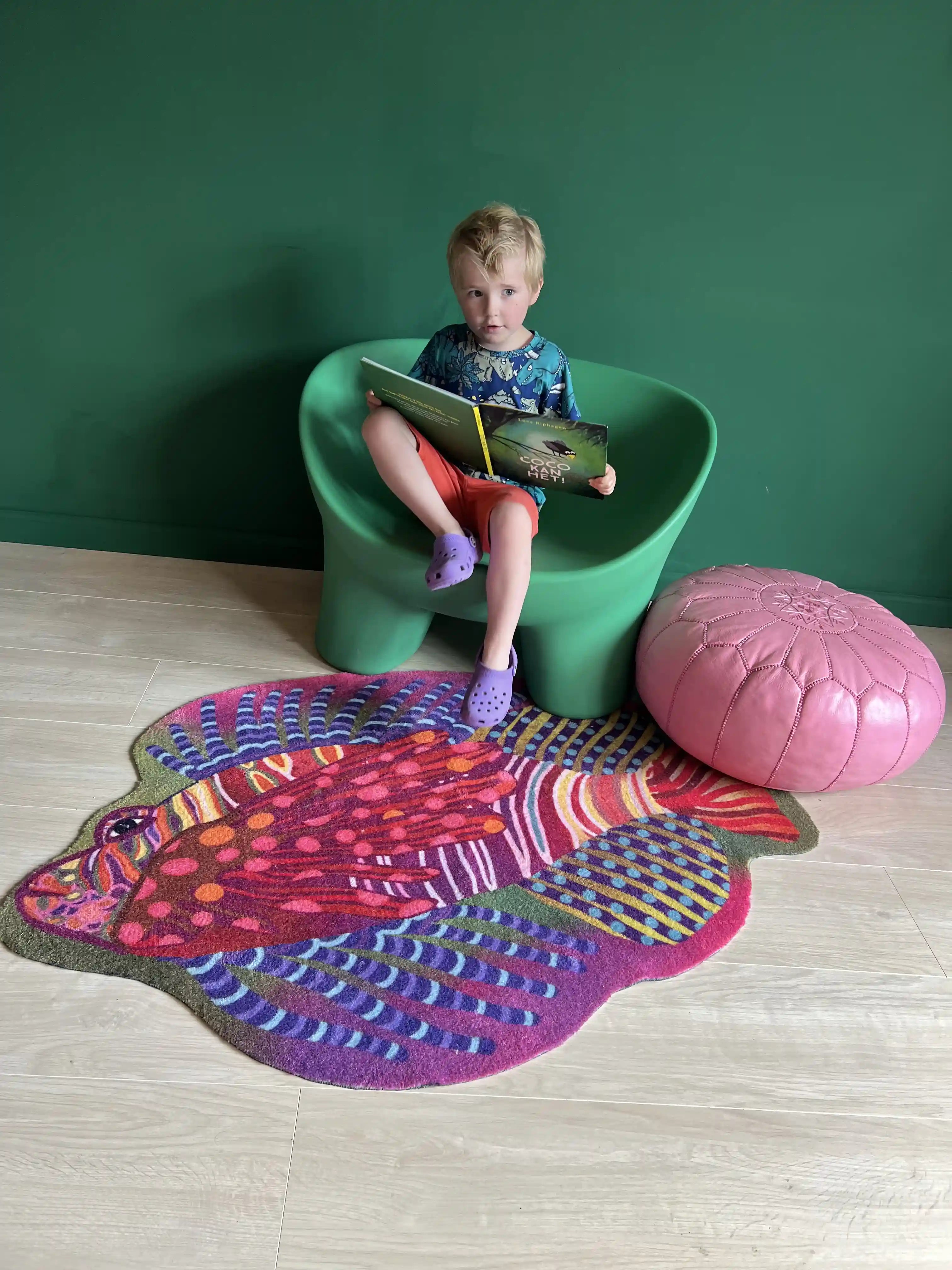 Zacht uitgesneden dierenkleed in de vorm van een koraalduivel van Studio LilaLine – het kleed toont een exotische vis met lange sierlijke vinnen en strepen, in een mix van roze, groen en blauw. De vorm is speels en dynamisch, met uitwaaierende lijnen die lijken te bewegen als onder water. Het kleed voelt zacht en luxe aan, ideaal als fantasierijke speelplek of knusse zitplek in de kinderkamer.