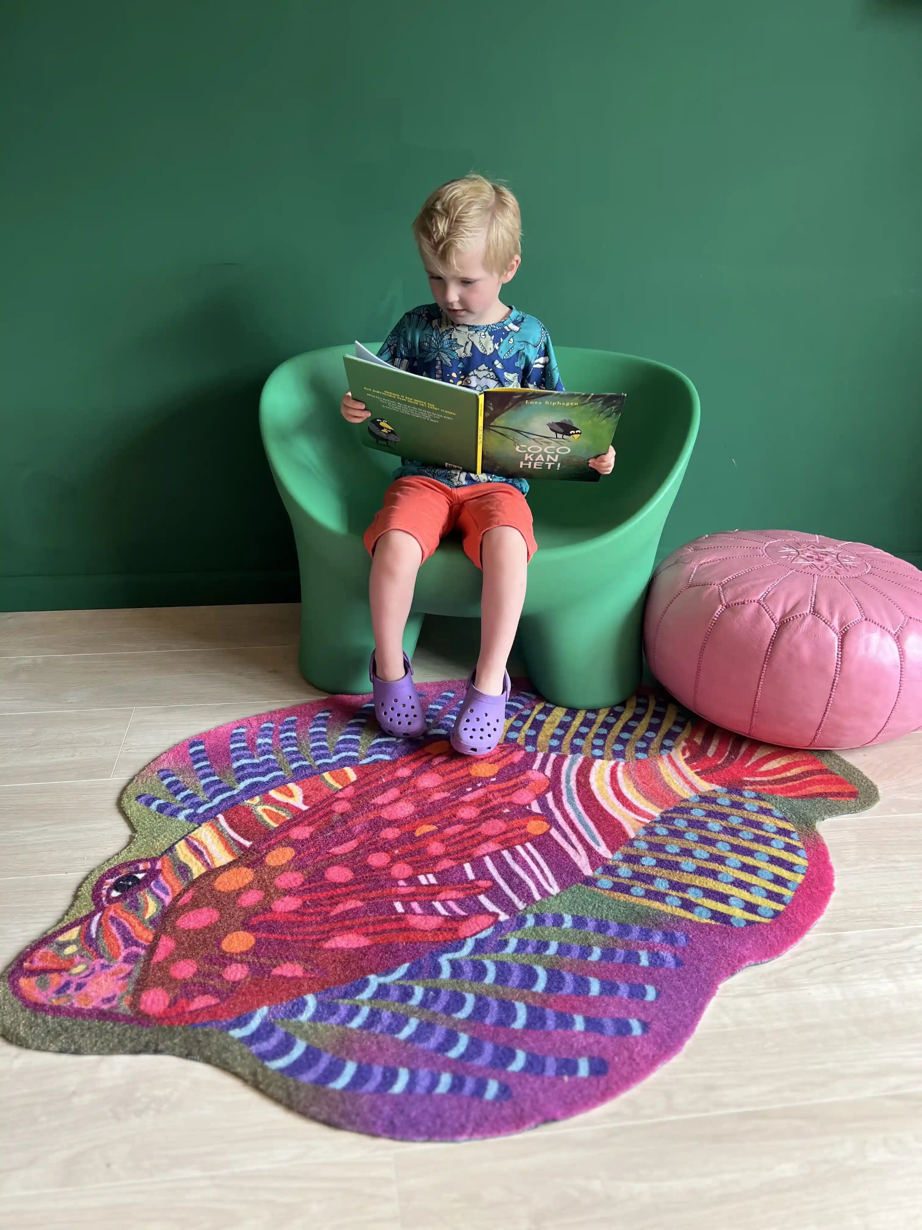 Zacht uitgesneden dierenkleed in de vorm van een koraalduivel van Studio LilaLine – het kleed toont een exotische vis met lange sierlijke vinnen en strepen, in een mix van roze, groen en blauw. De vorm is speels en dynamisch, met uitwaaierende lijnen die lijken te bewegen als onder water. Het kleed voelt zacht en luxe aan, ideaal als fantasierijke speelplek of knusse zitplek in de kinderkamer.