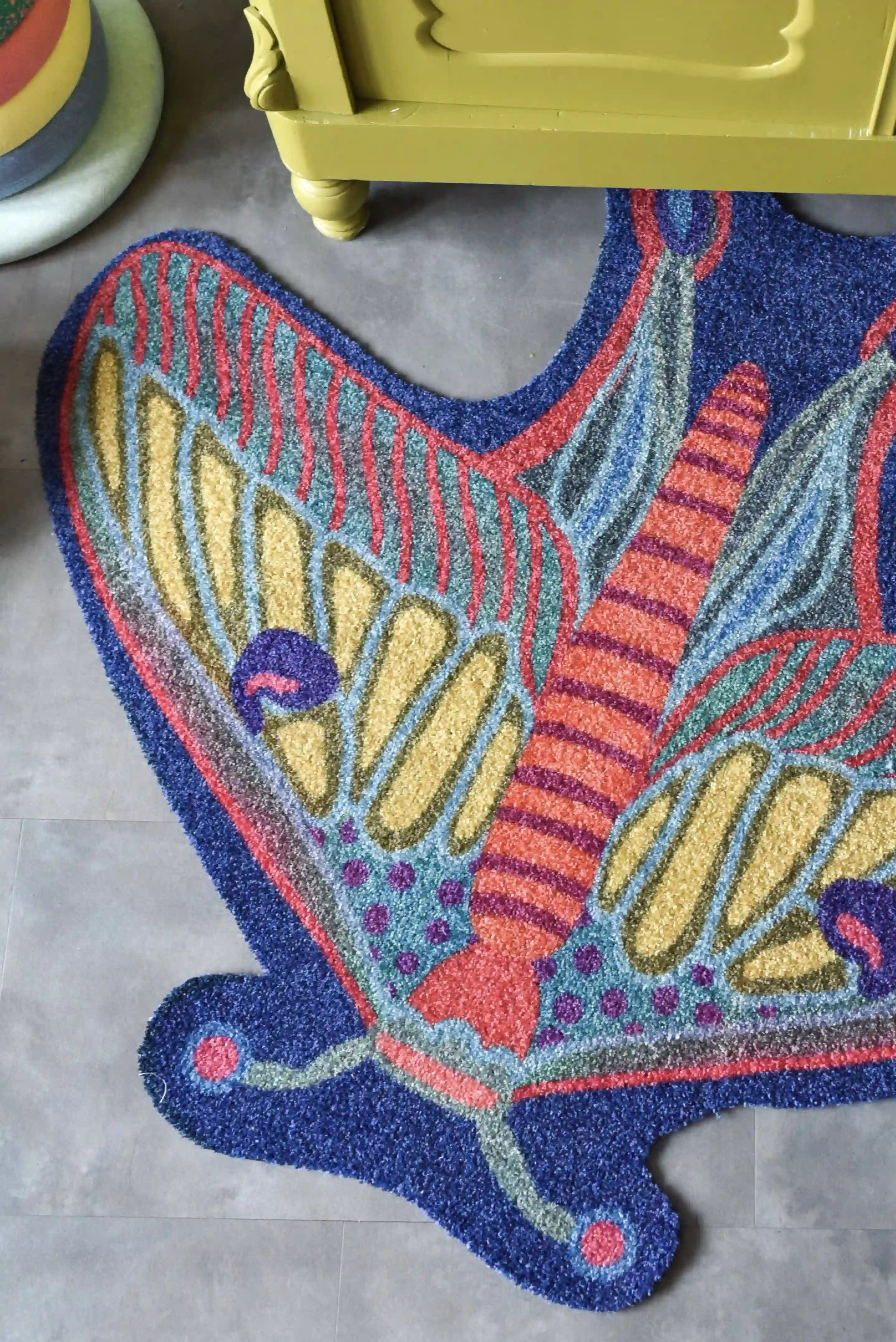 Zacht uitgesneden dierenkleed in de vorm van een nachtvlinder van Studio LilaLine – het kleed heeft uitgespreide vleugels in tinten van blauw, groen en fel oranje, met een patroon dat doet denken aan oogvormige vlekken en fijne lijnen. De vorm is symmetrisch en sierlijk, met zachte rondingen en een elegante uitstraling. Perfect om op te spelen of knus op te zitten in een kinderkamer of leeshoek.