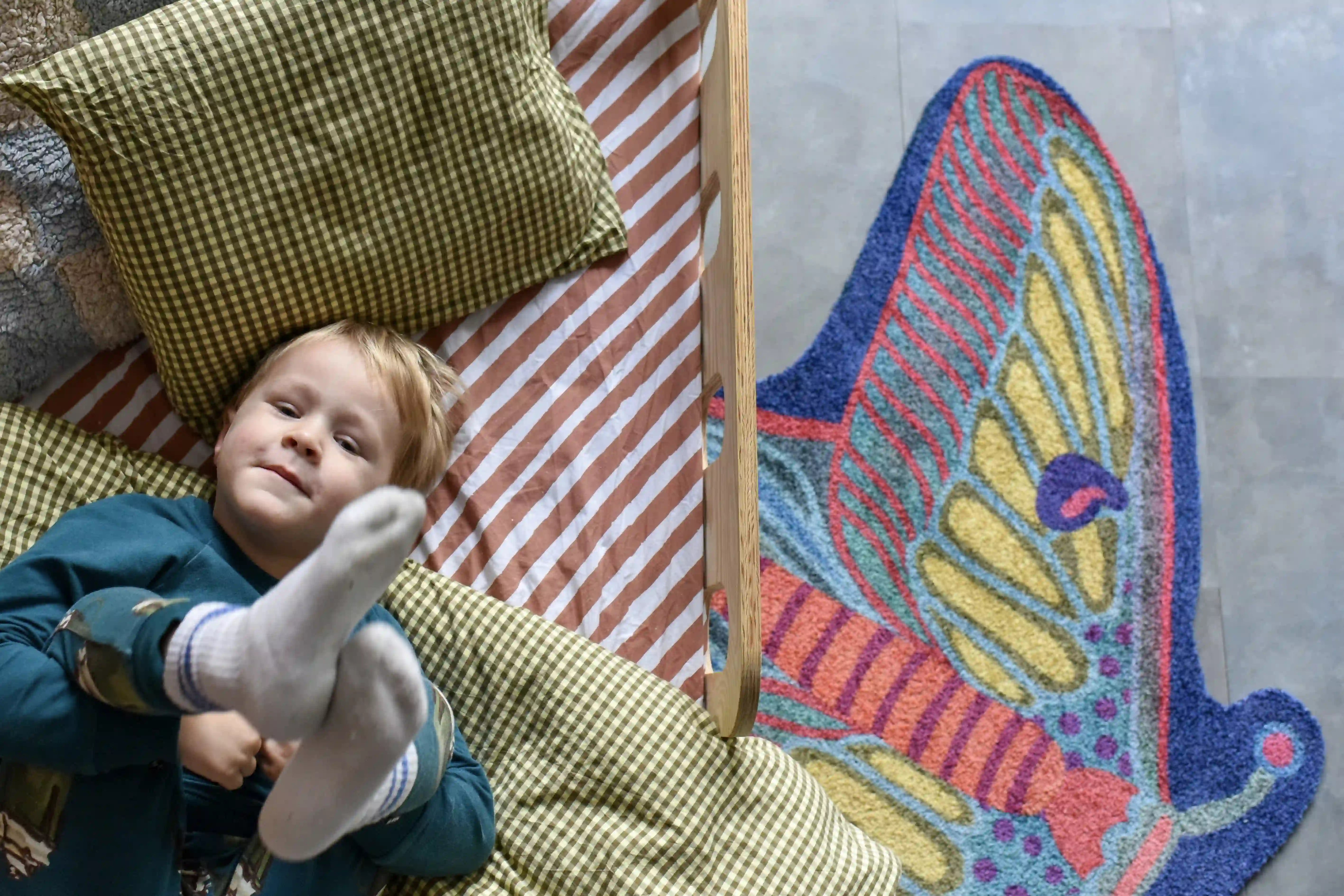 Zacht uitgesneden dierenkleed in de vorm van een nachtvlinder van Studio LilaLine – het kleed heeft uitgespreide vleugels in tinten van blauw, groen en fel oranje, met een patroon dat doet denken aan oogvormige vlekken en fijne lijnen. De vorm is symmetrisch en sierlijk, met zachte rondingen en een elegante uitstraling. Perfect om op te spelen of knus op te zitten in een kinderkamer of leeshoek.