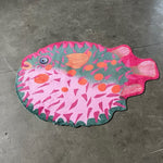 Zacht uitgesneden dierenkleed in de vorm van een kogelvis van Studio LilaLine – het kleed toont een ronde vis met grappige stekelvormen, uitgevoerd in frisse roze en groentinten. De vis heeft een vriendelijke uitstraling met een bolle buik en sprekende ogen. Het oppervlak is zacht en comfortabel, perfect om op te spelen of lekker te zitten in een speelhoek of kinderkamer.