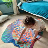 Zacht uitgesneden dierenkleed in de vorm van een koraalduivel van Studio LilaLine – deze fantasierijke vis heeft sierlijke vinnen die wijd uitstaan, in sprekende tinten groen en oranje. De visvorm is dynamisch en decoratief, met speelse strepen en zachte rondingen. Het kleed is heerlijk zacht en nodigt uit tot spelen, liggen of fantaseren in een gezellige hoek van de kinderkamer.