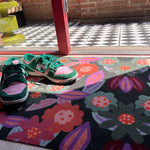 Droogloopmat en deurmat van Studio LilaLine met een speelse bloemvorm in tinten roze, oranje en groen – het ontwerp doet denken aan een vrolijk uitgestoken koekje met een knipoog naar retro bloemmotieven. De mat is slijtvast, neemt goed vocht op en zorgt voor een kleurrijke en uitnodigende entree, zowel praktisch als decoratief.