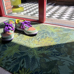 Droogloopmat en deurmat van Studio LilaLine met een print die doet denken aan een dichtbegroeid, fris groen bos – opgebouwd uit allerlei groentinten en abstracte bladerstructuren. De mat straalt rust en natuur uit, en is slijtvast en vochtopnemend. Ideaal om je hal of gang een kalme, organische uitstraling te geven met een vleugje avontuur.