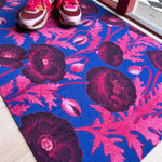 Droogloopmat met roze klaprozen die oplichten tegen een felblauwe achtergrond. Een verrassende winterprint vol kleur en optimisme.