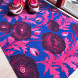 Droogloopmat met roze klaprozen die oplichten tegen een felblauwe achtergrond. Een verrassende winterprint vol kleur en optimisme.