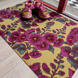 Droogloopmat met roze stokrozen op een warme okergele achtergrond. Een vrolijke lentemix die meteen zon en bloemen de hal binnenbrengt.