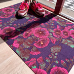 Droogloopmat met roze stokrozen op een diepe paarse ondergrond. Een rijke, zomerse print vol charme en contrast.
