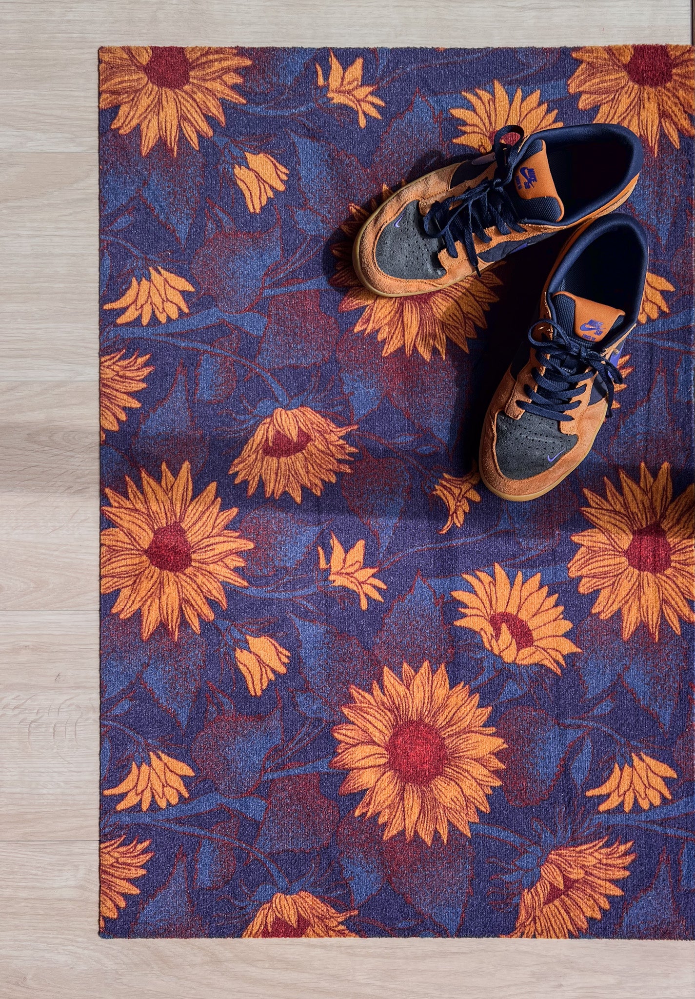 Droogloopmat met okergele zonnebloemen op een diepe donkerblauwe ondergrond. Een krachtige, winterse bloemenprint die sfeer en warmte brengt bij binnenkomst.
