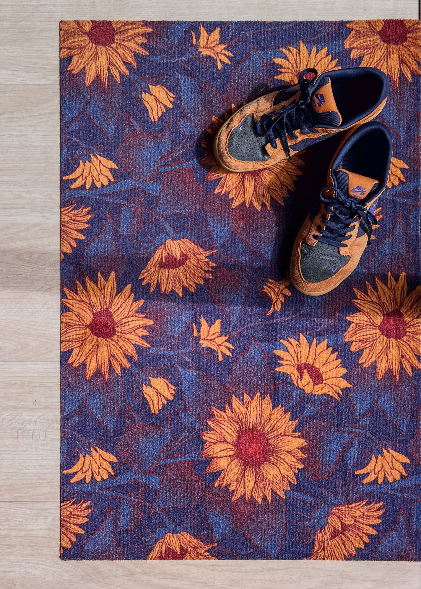 Droogloopmat met okergele zonnebloemen op een diepe donkerblauwe ondergrond. Een krachtige, winterse bloemenprint die sfeer en warmte brengt bij binnenkomst.