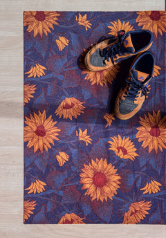 Droogloopmat met okergele zonnebloemen op een diepe donkerblauwe ondergrond. Een krachtige, winterse bloemenprint die sfeer en warmte brengt bij binnenkomst.