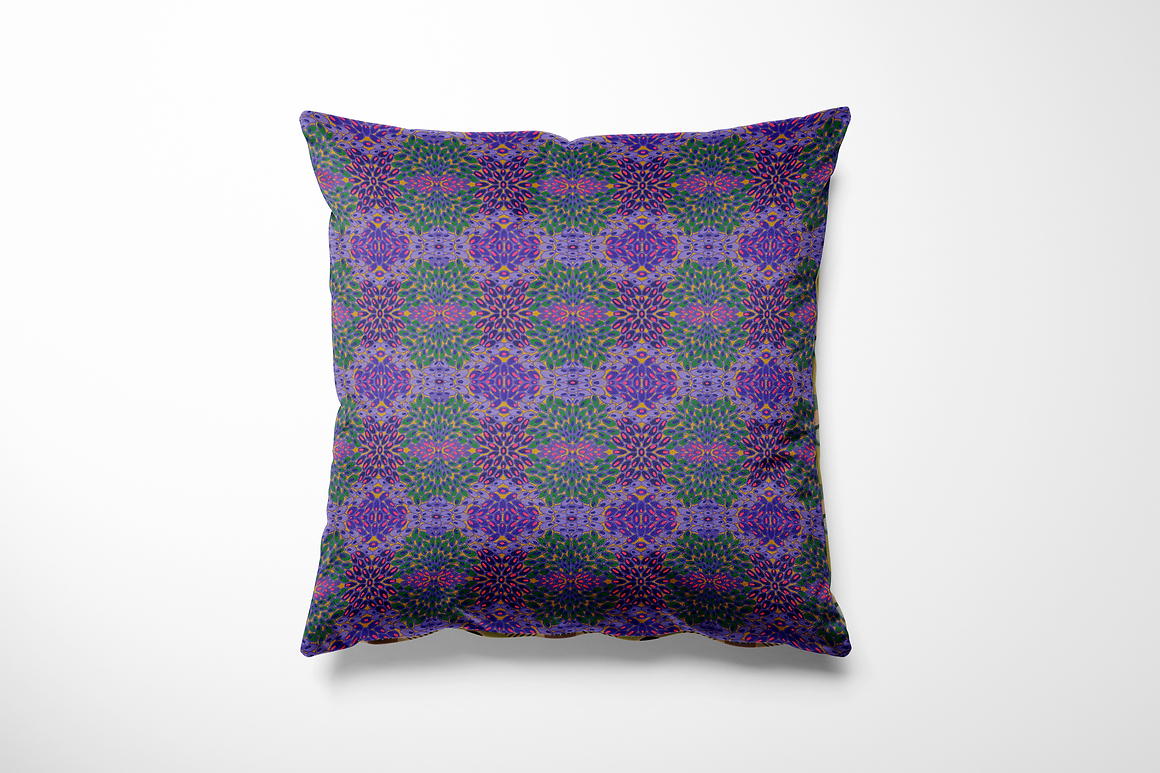 Vierkant binnen- en buitenkussen met een herhalend bloemenpatroon in een caleidoscopisch effect. De print bestaat uit paarse, roze en hot pink bloemblaadjes met accenten in groen, blauw en oranje, geplaatst op een zacht paarse achtergrond. Het geheel geeft een levendige en speelse uitstraling aan je tuinset, bank of loungehoek.