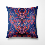 Vierkant binnen- en buitenkussen met een verfijnde symmetrische bloemenprint in rood, roze, lila en paars, met sierlijke takken en blaadjes die lijken te dansen over een diepe kobaltblauwe achtergrond. De print bevat ook kleine gele stipjes als accent. Een elegante eyecatcher die kleur en karakter toevoegt aan je tuinbank of woonkamer.