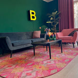 Luxe vloerkleed Diamond Pink van Studio LilaLine met een grafisch diamantpatroon in roze, groen en subtiele goudtinten – het kleed voelt zacht maar stevig aan, en het patroon bestaat uit ritmische vormen die in lagen over elkaar lijken te schuiven, alsof je naar een fonkelende caleidoscoop kijkt. De kleuren zijn warm, levendig en geven het kleed een rijke en speelse uitstraling.